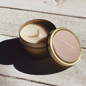 Candle in a gold tin with a pink label on a wooden surface