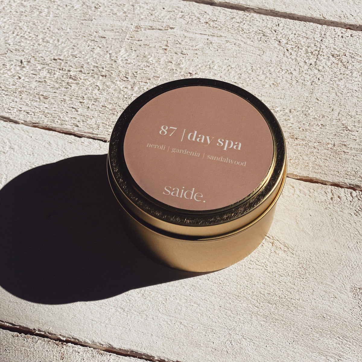 Gold candle jar with '87 day spa' label on a light wooden surface