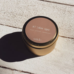 Gold candle jar with '87 day spa' label on a light wooden surface
