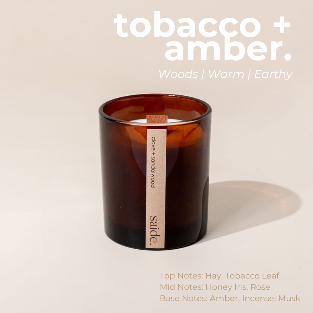 Brown candle with a label on a beige background, featuring the scent 'tobacco + amber'.
