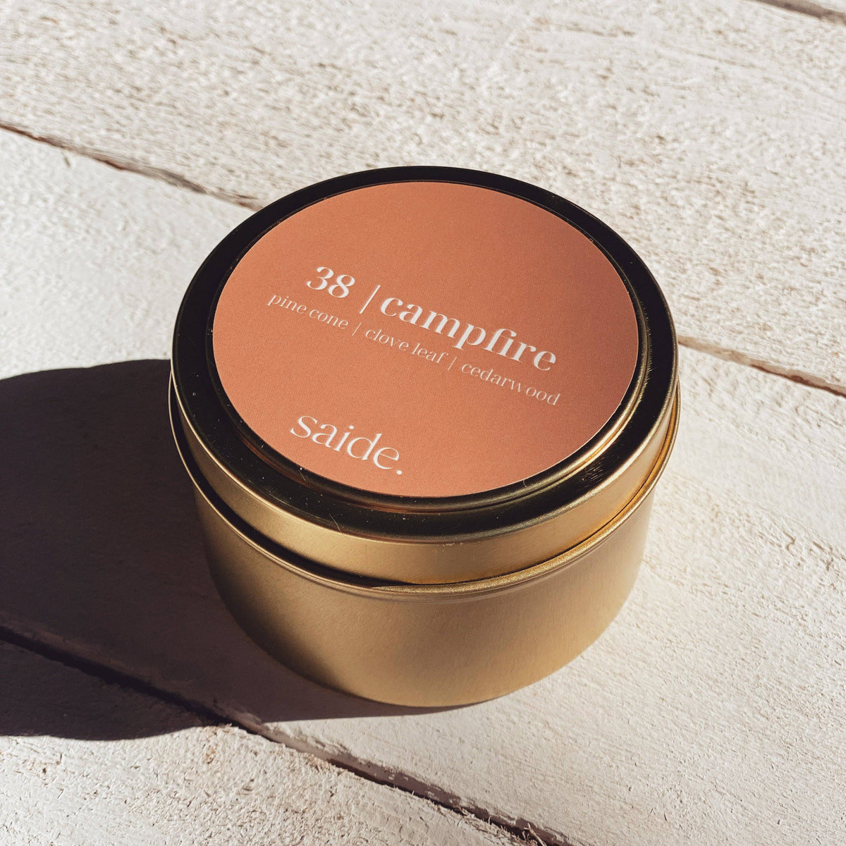 Gold candle jar with '38 Campfire' scent on a light stone surface