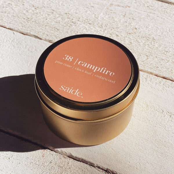 Gold candle jar with '38 Campfire' scent on a light stone surface