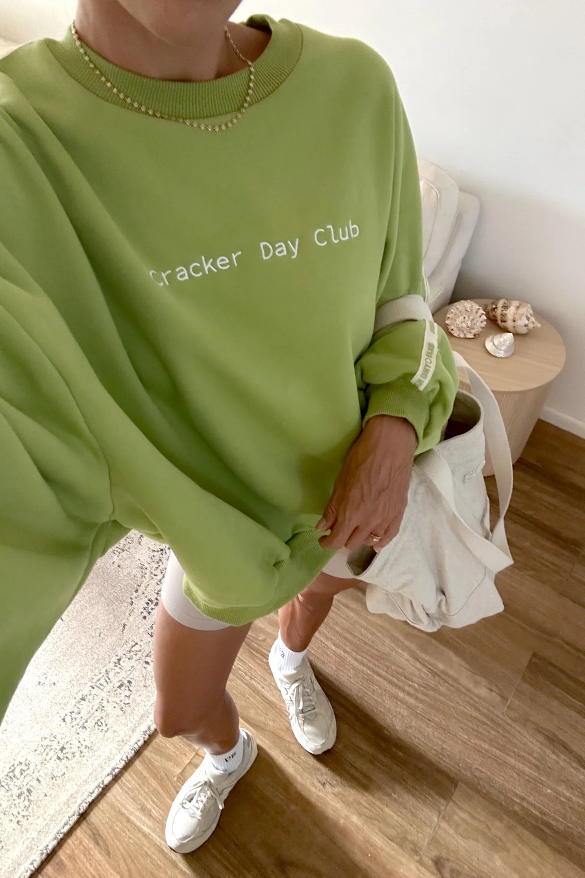 Person wearing a green sweatshirt with 'Cracker Day Club' text, standing in a room with wooden floor and white walls.