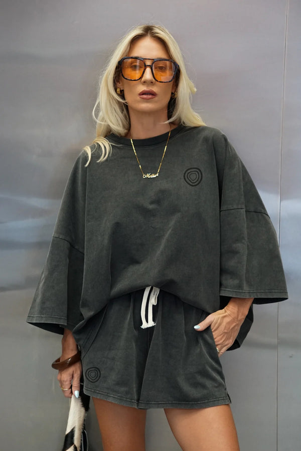 Person wearing a dark green oversized sweater and shorts set with sunglasses against a neutral background