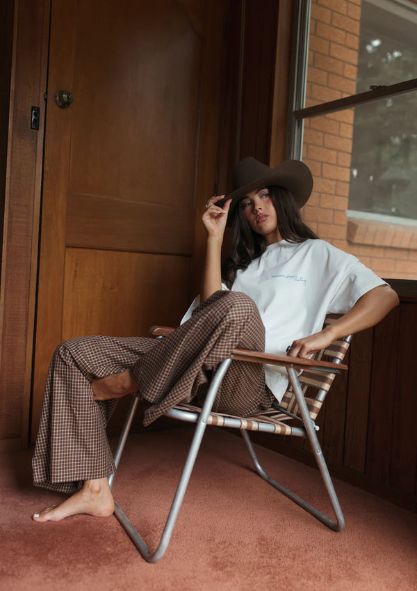 Women sitting in a chair wearing cowboy hat, white tee and FAR MER by Whitney Boyfriend Plaid Pants ALL MY EXES