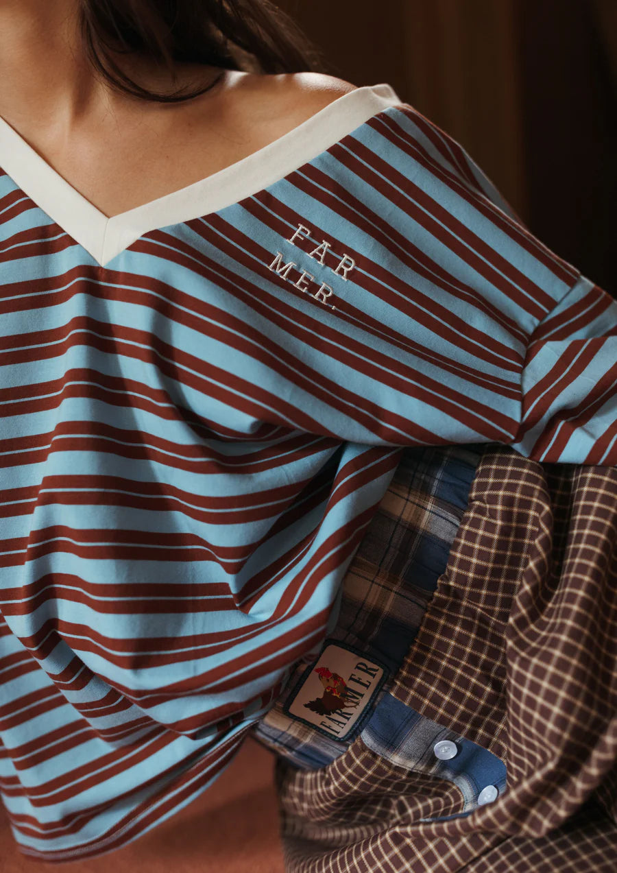 Close up of a woman sitting wearing blue stripe tee and plaid pants from FAR MER by Whitney in a beige room 