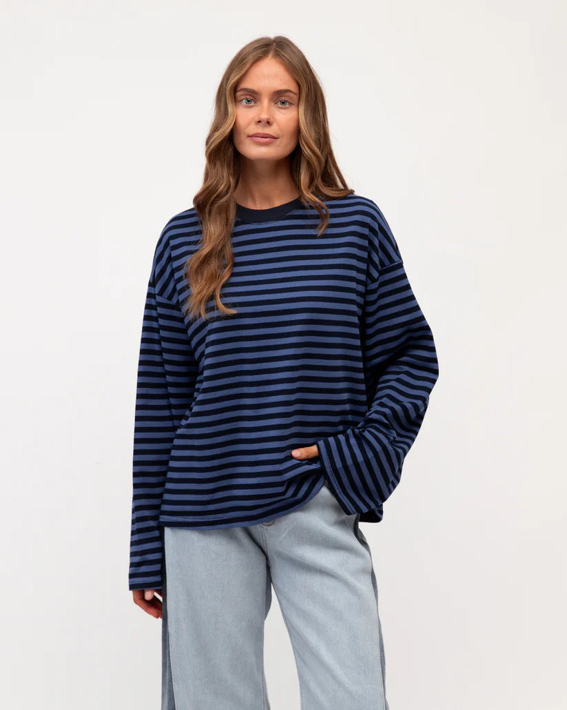 Woman wearing a blue and black striped sweater with light gray pants on a white background
