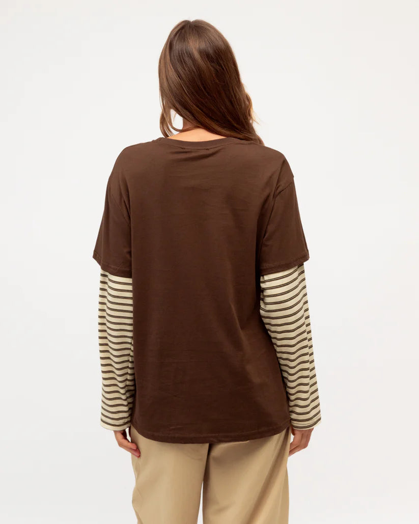 Person wearing a brown shirt with striped sleeves on a plain background