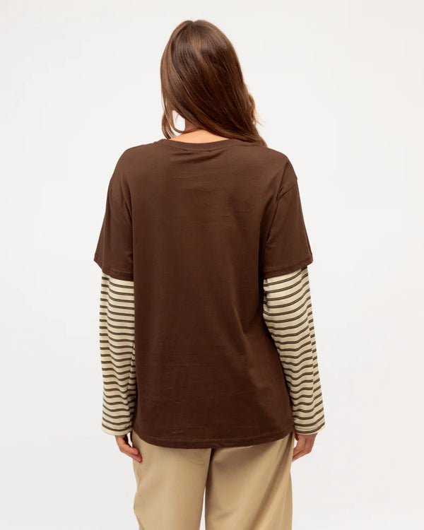 Person wearing a brown shirt with striped sleeves on a plain background