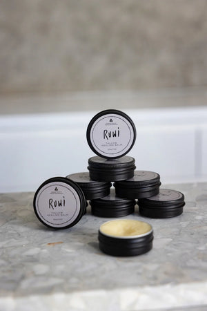 7 tins of Ruwi tallow balm stacked up ontop of each other on a kitchen bench, with one at the front open to show the product inside