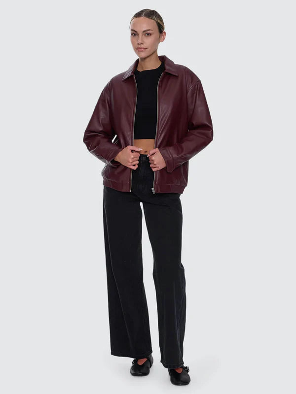 Person wearing a burgundy leather jacket and black pants on a white background