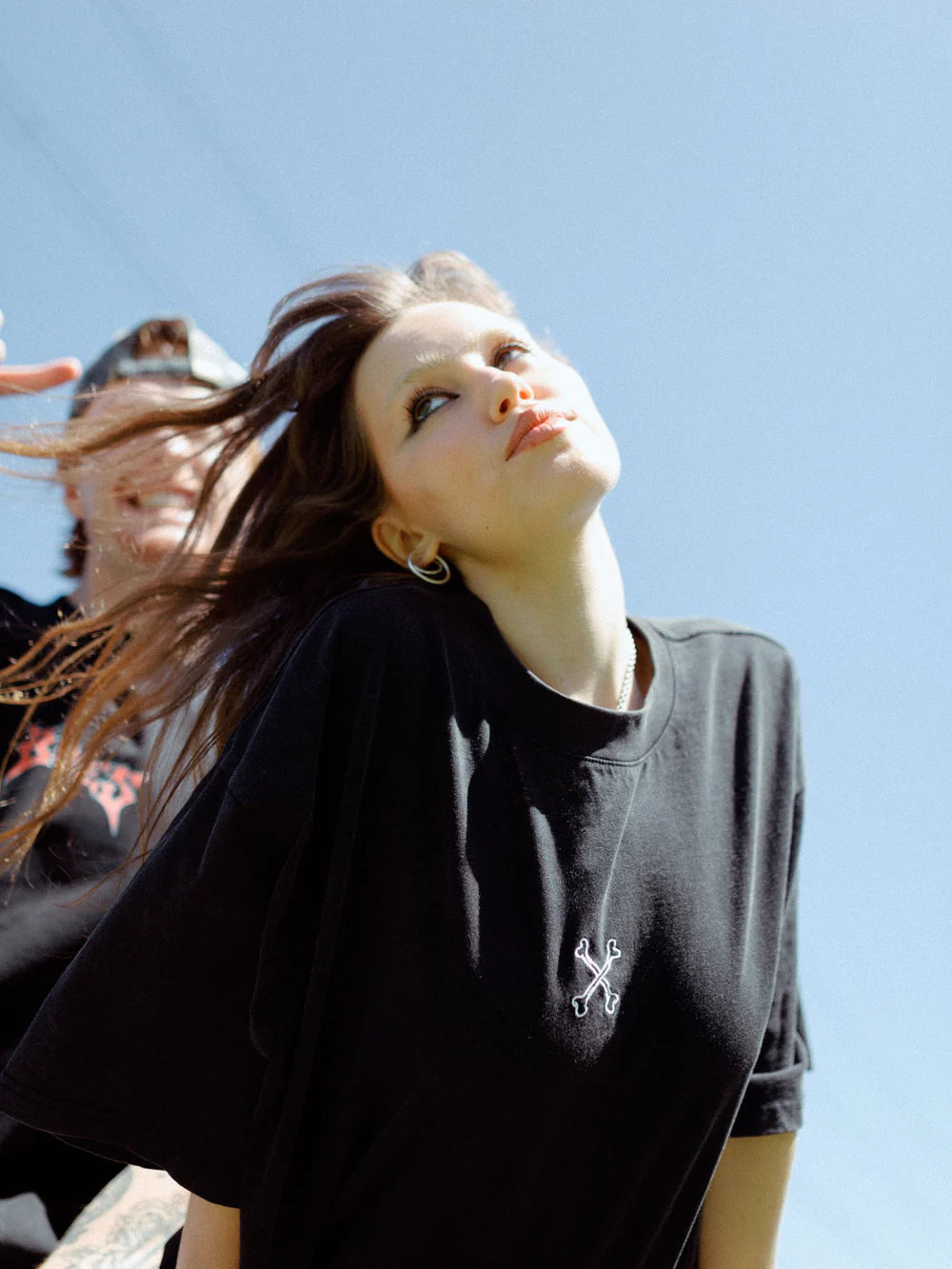 Person wearing a black t-shirt with a white logo against a clear blue sky