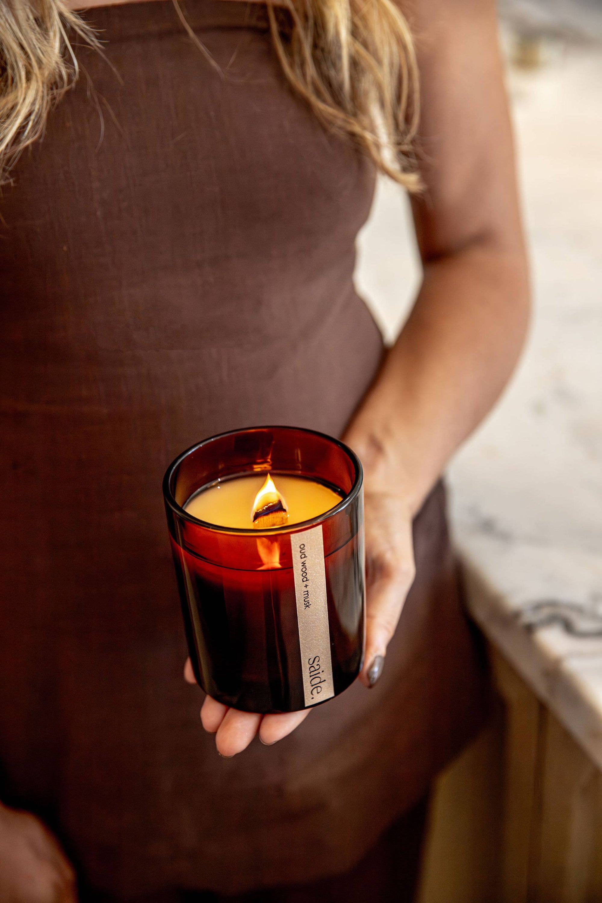 Person holding a lit candle in a dark container with 'SOM' branding.