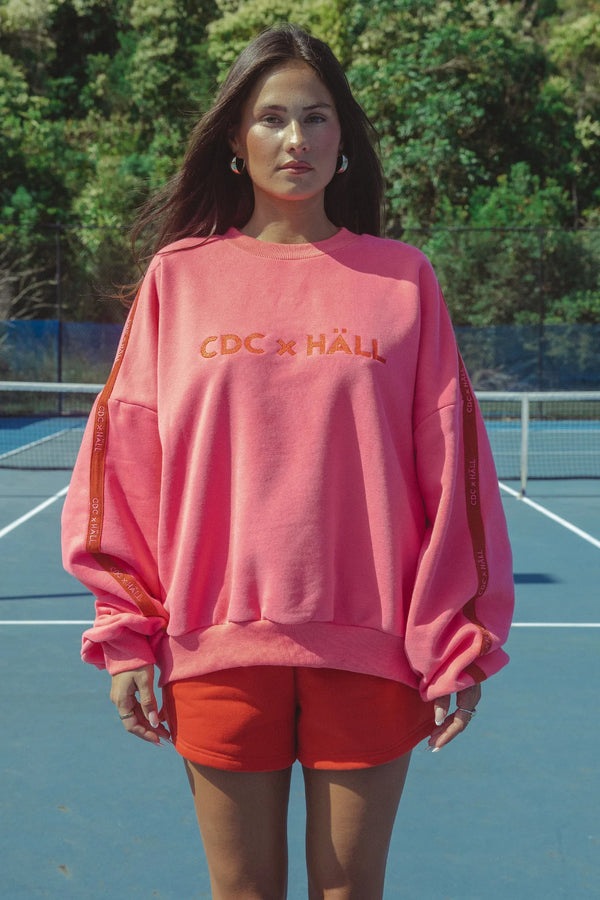 Person wearing a pink sweatshirt with text on a tennis court