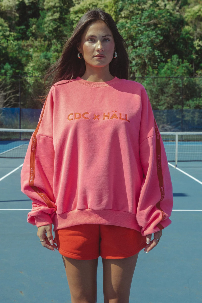 Person wearing a pink sweatshirt with text on a tennis court