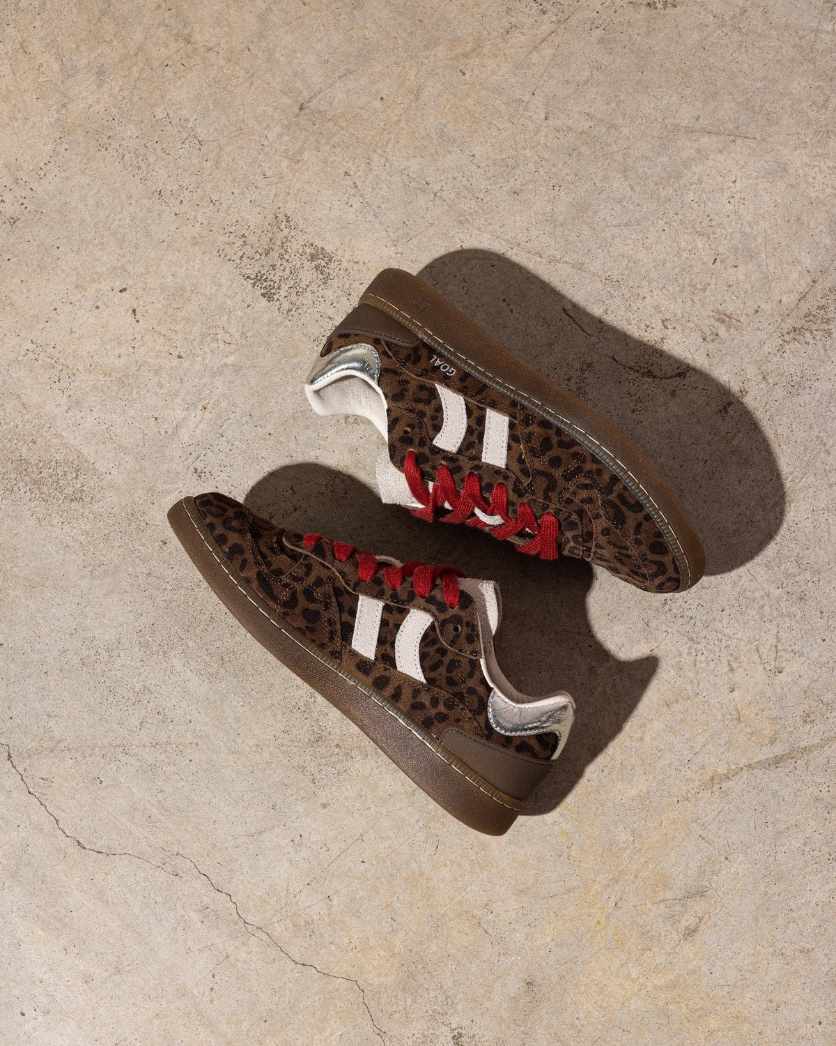 Pair of brown sneakers with leopard print pattern on a beige stone surface