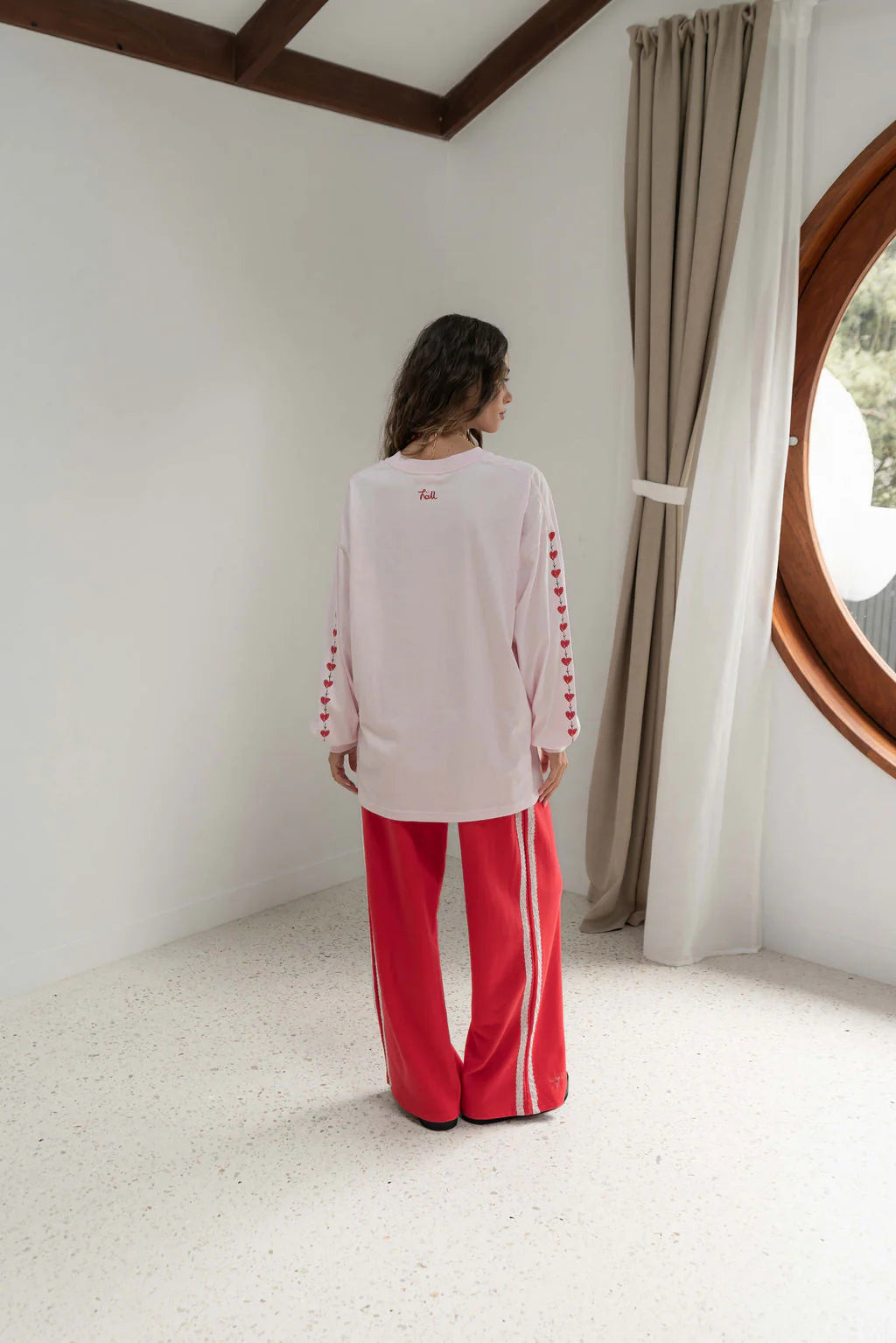 back view of a woman wearing a pink long sleeve tee with red hearts down the sleeve and red pants.