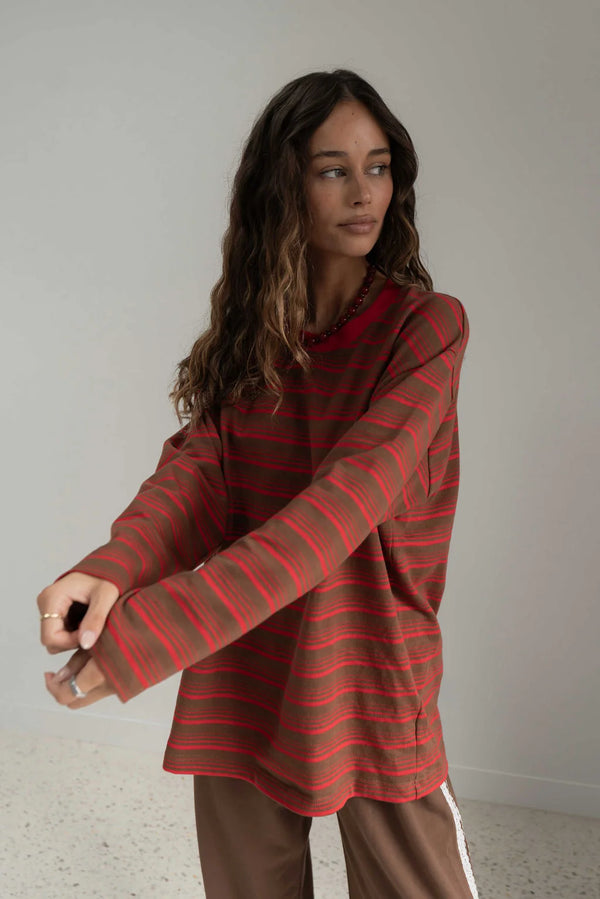 girl wearing long sleeve red and brown striped tee against white wall
