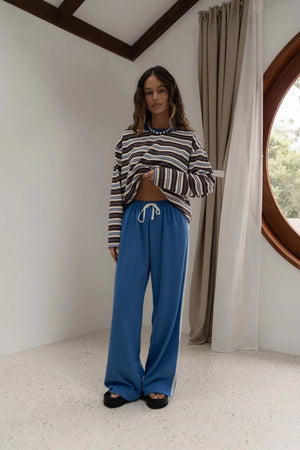 woman standing near window wearing brown white and blue stripe long sleeve tee and blue pants with lace trim