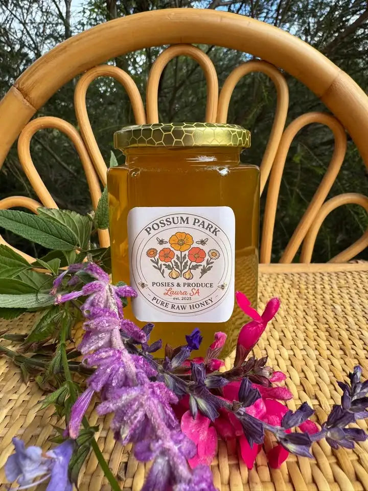Jar of Possum Park honey on a wicker chair with flowers and leaves.