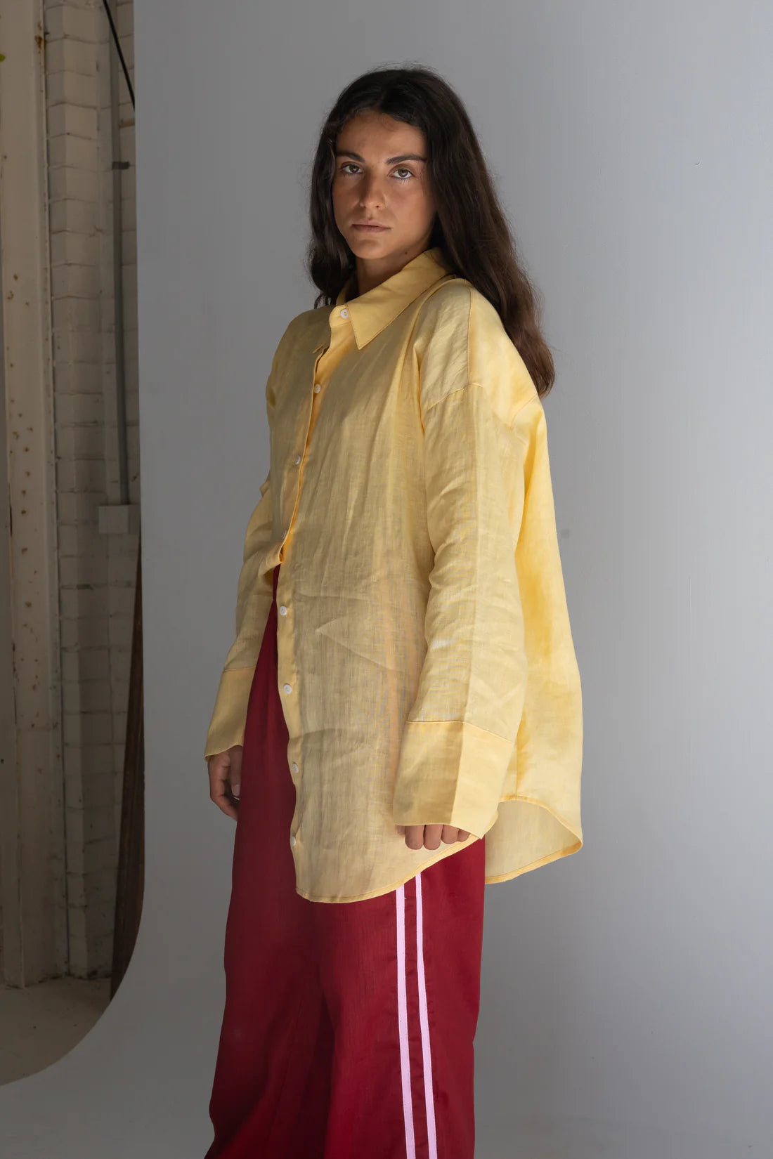 girl standing near wall wearing crimson linen pants and yellow linen shirt
