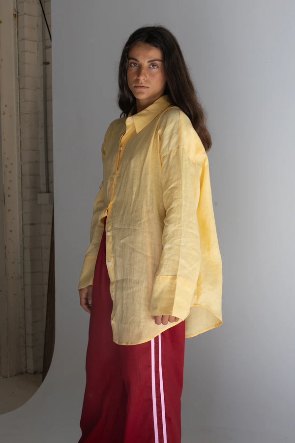 girl standing near wall wearing crimson linen pants and yellow linen shirt