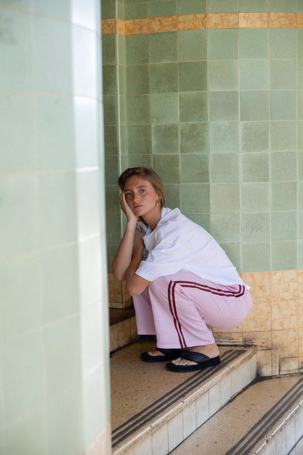 girl crouched down on steps of shops wearing pale fuschia pants, white t-shirt and black thongs
