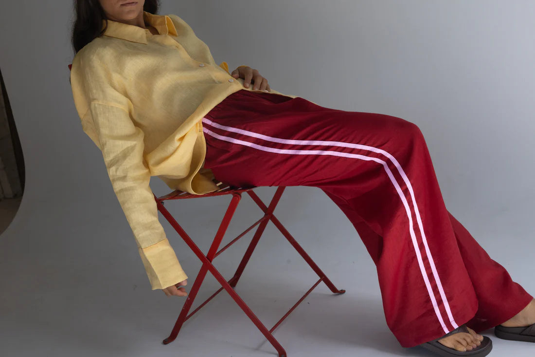 person sitting on red seat wearing crimson pants with pink stripe, and yellow linen shirt