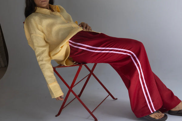 person sitting on red seat wearing crimson pants with pink stripe, and yellow linen shirt
