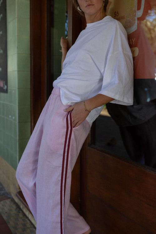 person wearing light coloured pants and a white tshirt, leaning against a shop window