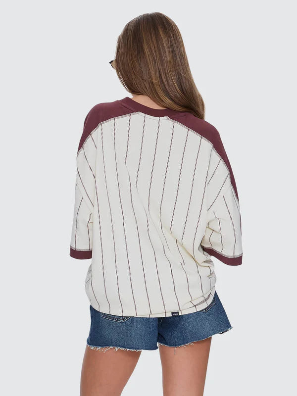 Person wearing a maroon and white striped baseball shirt with denim shorts on a plain background